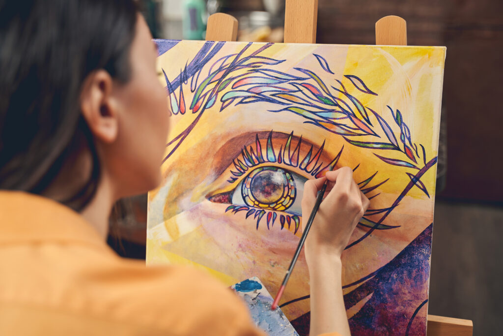 Close up of talented female artist drawing colorful beautiful picture with paints in home workshop