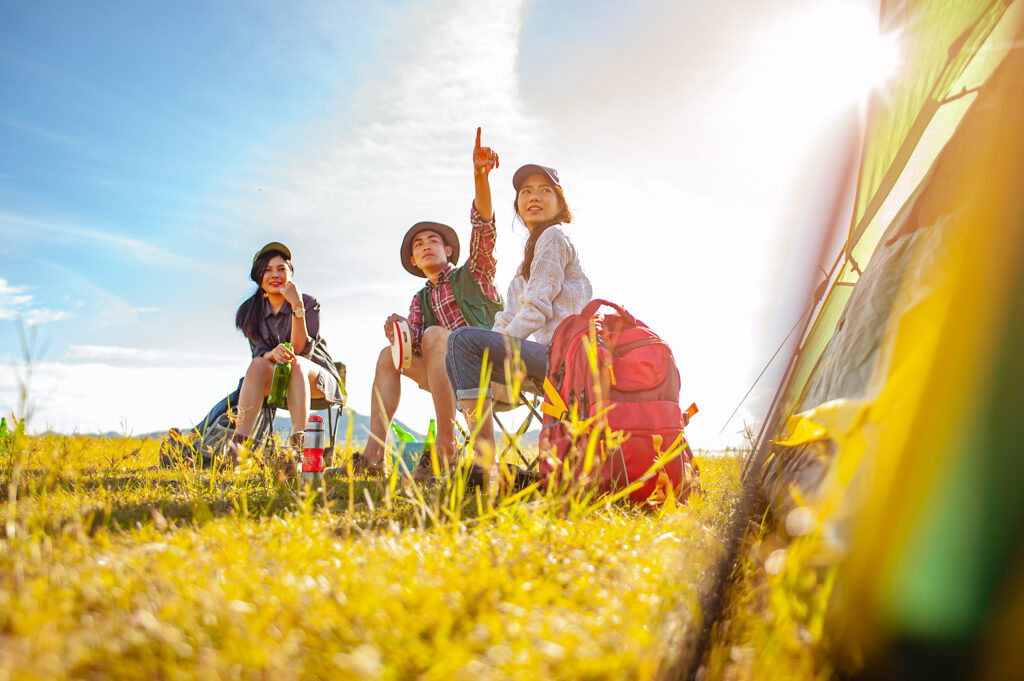 Team of asian climbers hiker are sitting and enjoying a drink after a set up outdoor tent in the forest path autumn season. Hiking, hiker, team, forest, camping , activity concept.