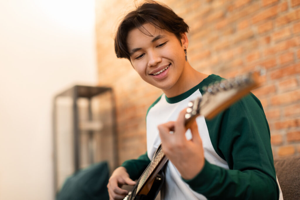 Young Musician. Cheerful Asian Teen Boy Playing Electric Guitar Having Fun At Home. Guy Learning To Play Instrument On Weekend. Musical Leisure And Hobby Concept. Selective Focus